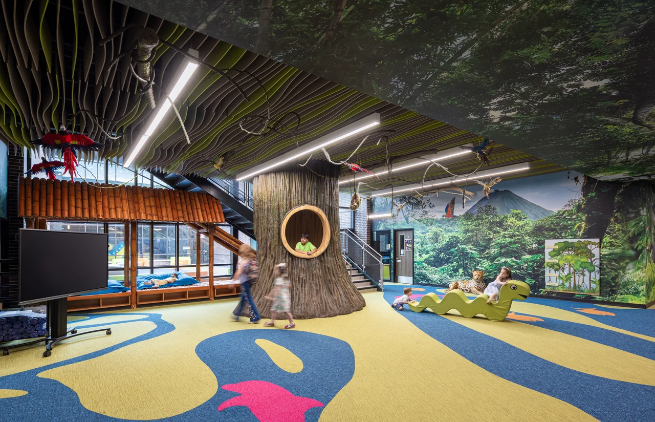 A tree trunk with an inset seat anchors a forest-themed learning area.