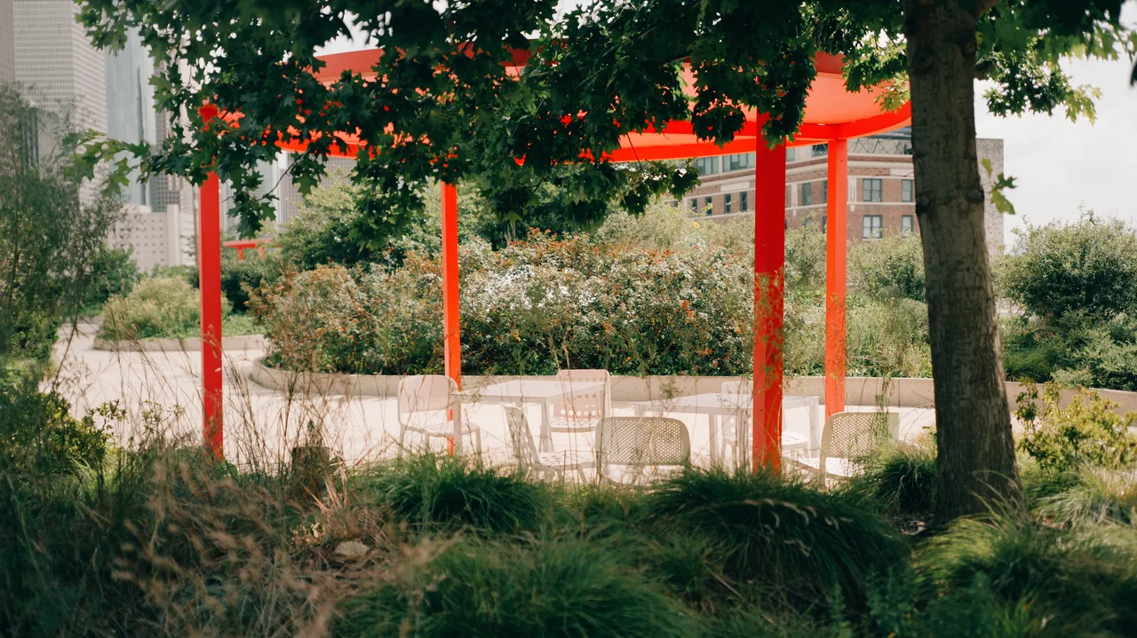 Red steel framing stands among trees and garden planting.