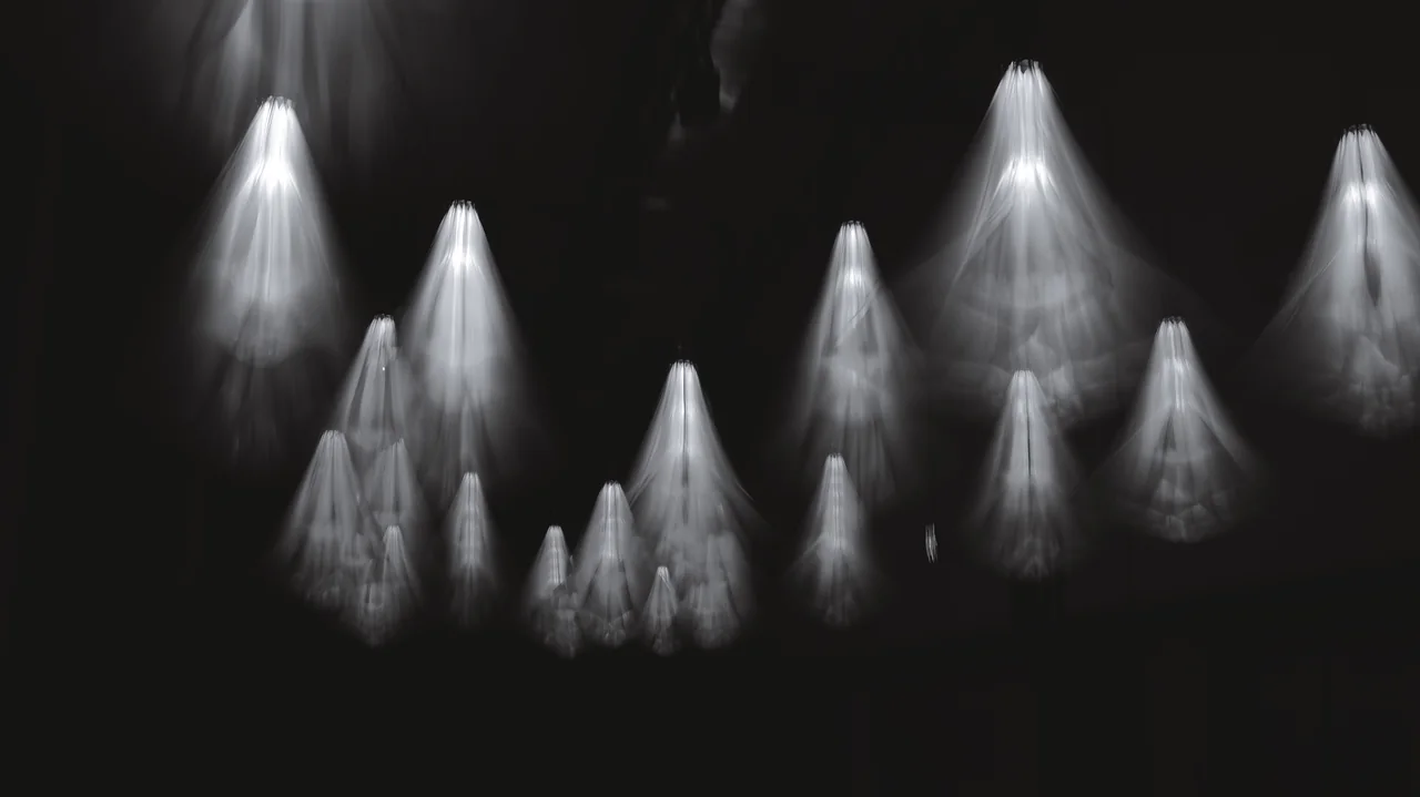 Cone-shaped beams of light form a pattern against a dark background.