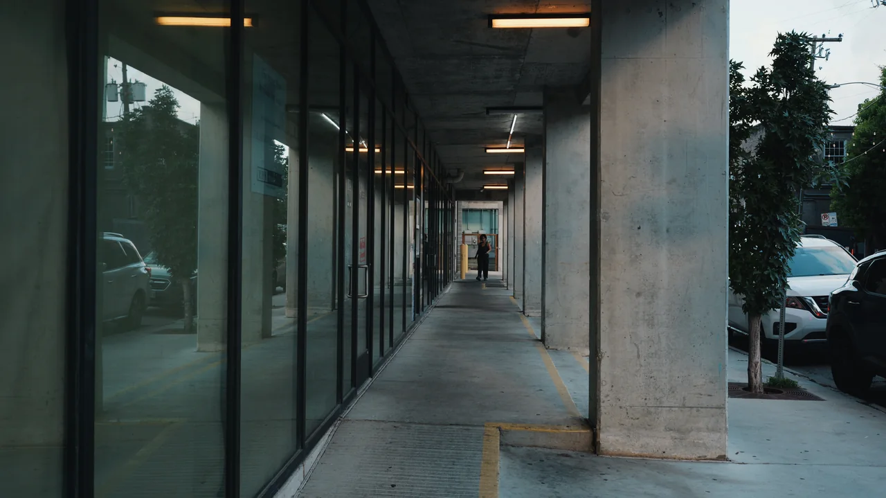 A concrete and glass walkway recedes through repeated structural bays.