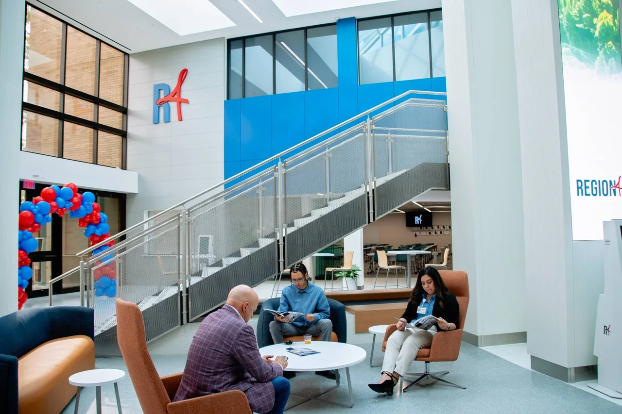 People gather in the renovated lobby beside stairs and a tall digital display.